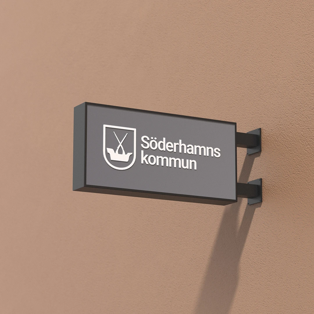 3D-illustration av en grå väggskylt fäst vid en brun vägg. Skylten har  Söderhamns kommun logotyp.